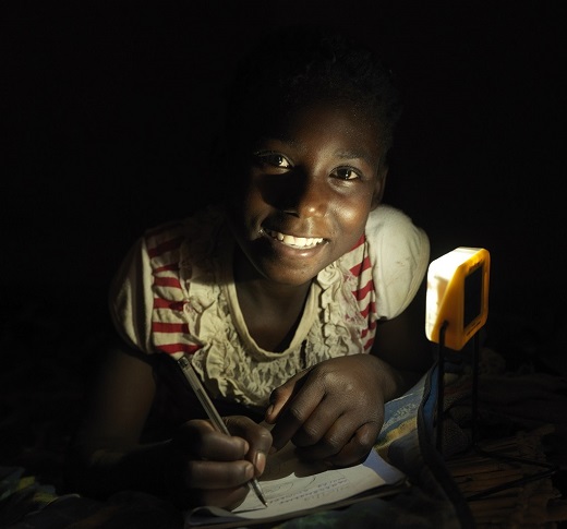 Agnesi looks to camera while completing her homework by solar light.