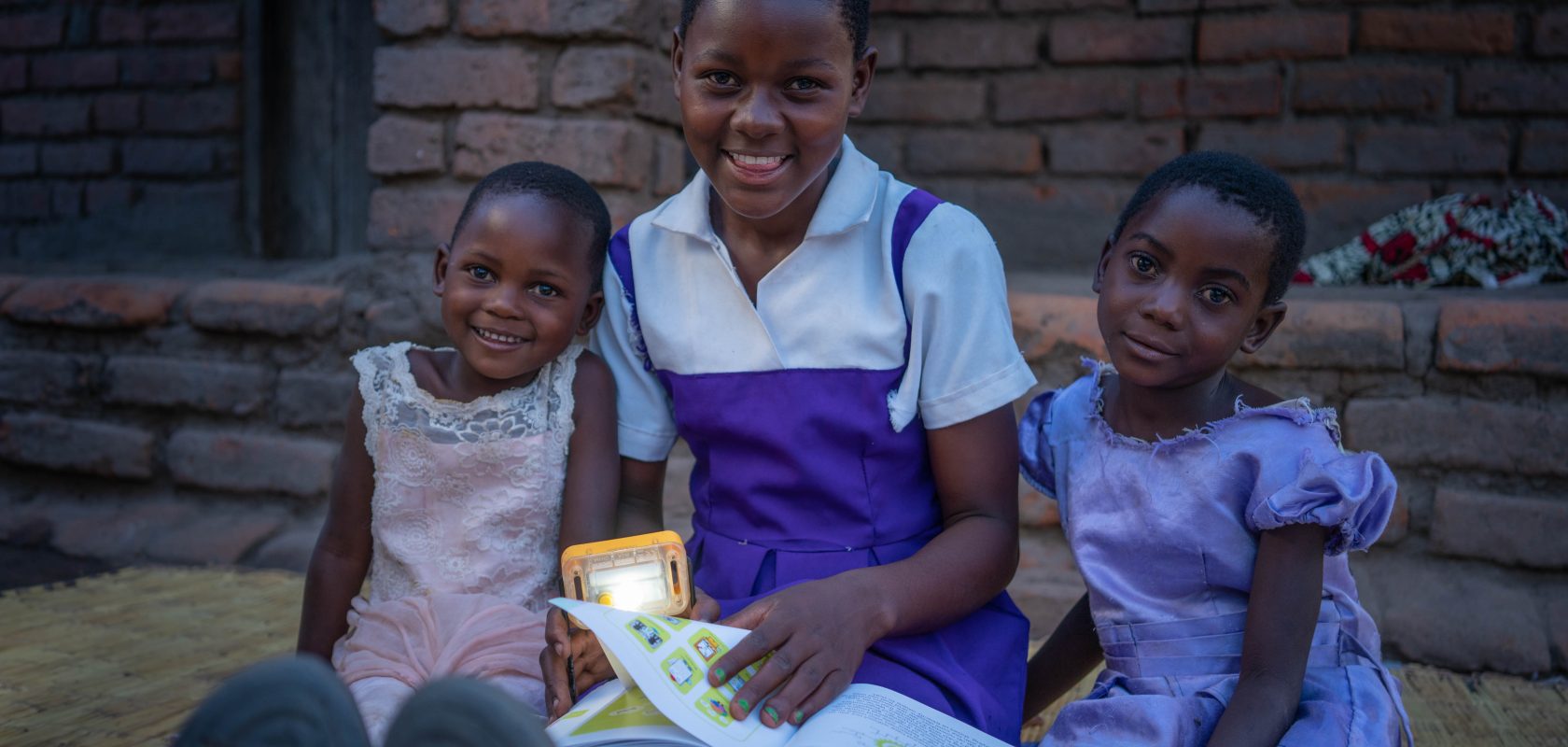 Fabiola, reads to her younger sisters using a solar light