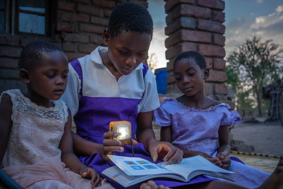 Fabriola reads to her sisters by the power of a solar light