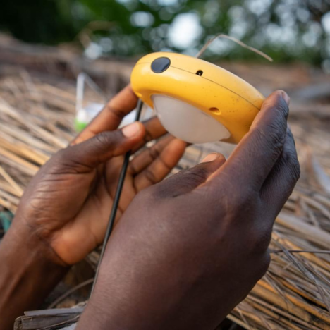 Eness Naliwa holding a solar light, and placing it on a straw roof