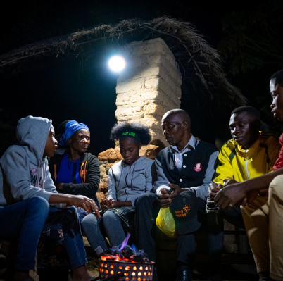 Simon Muchinga sits with his family under the glow of a solar light
