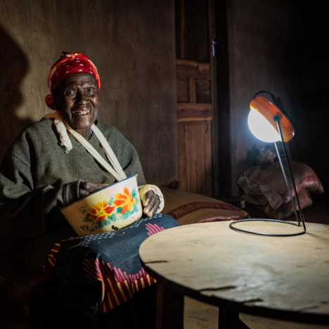 Moderster Sinyolo is sitting at her table, holding a bowl with a flower pattern, under the glow of her solar light on a table.