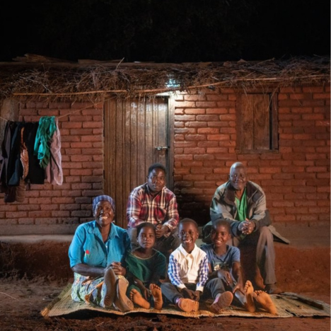 John and his family sit outside their home under a solar light