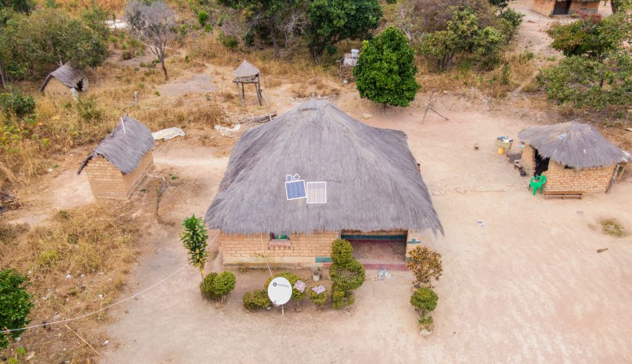 Drone photo of a thatched roof hut in Zambia with a solar panel on the roof.